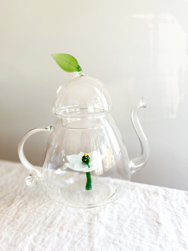 clear hand blown glass teapot with white glass lotus flower in bottom on table