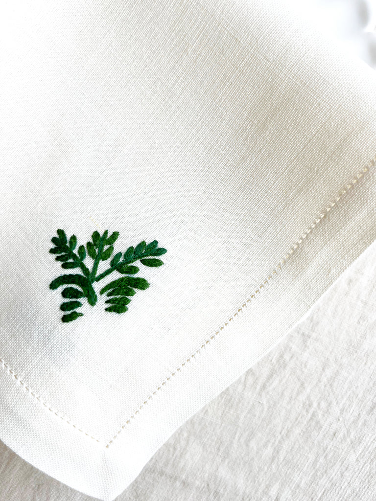 white hand embroidered linen napkins with dark green leaves in corner 16 inches square edge detail view