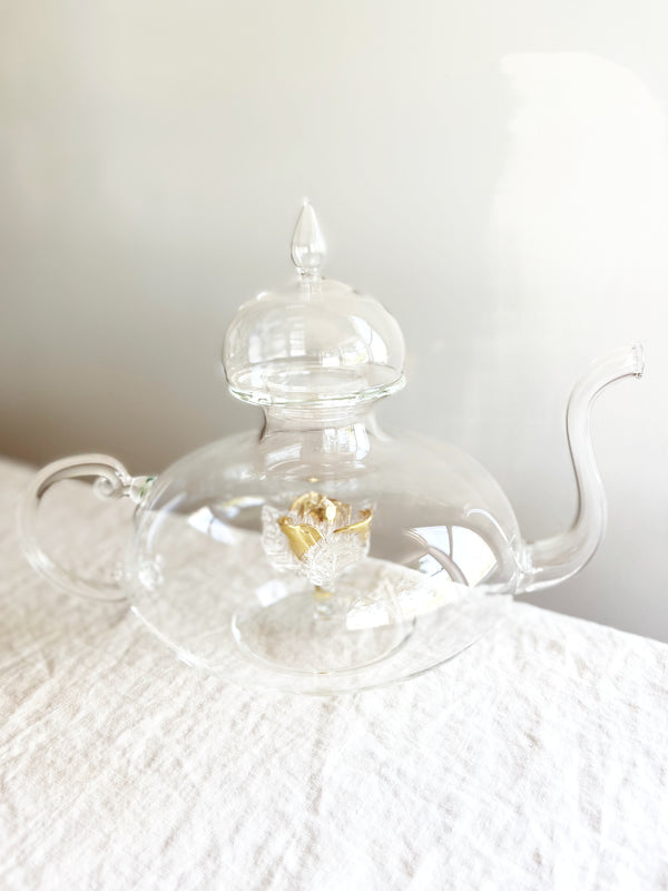 clear hand blown glass teapot with gold glass rose in bottom on table