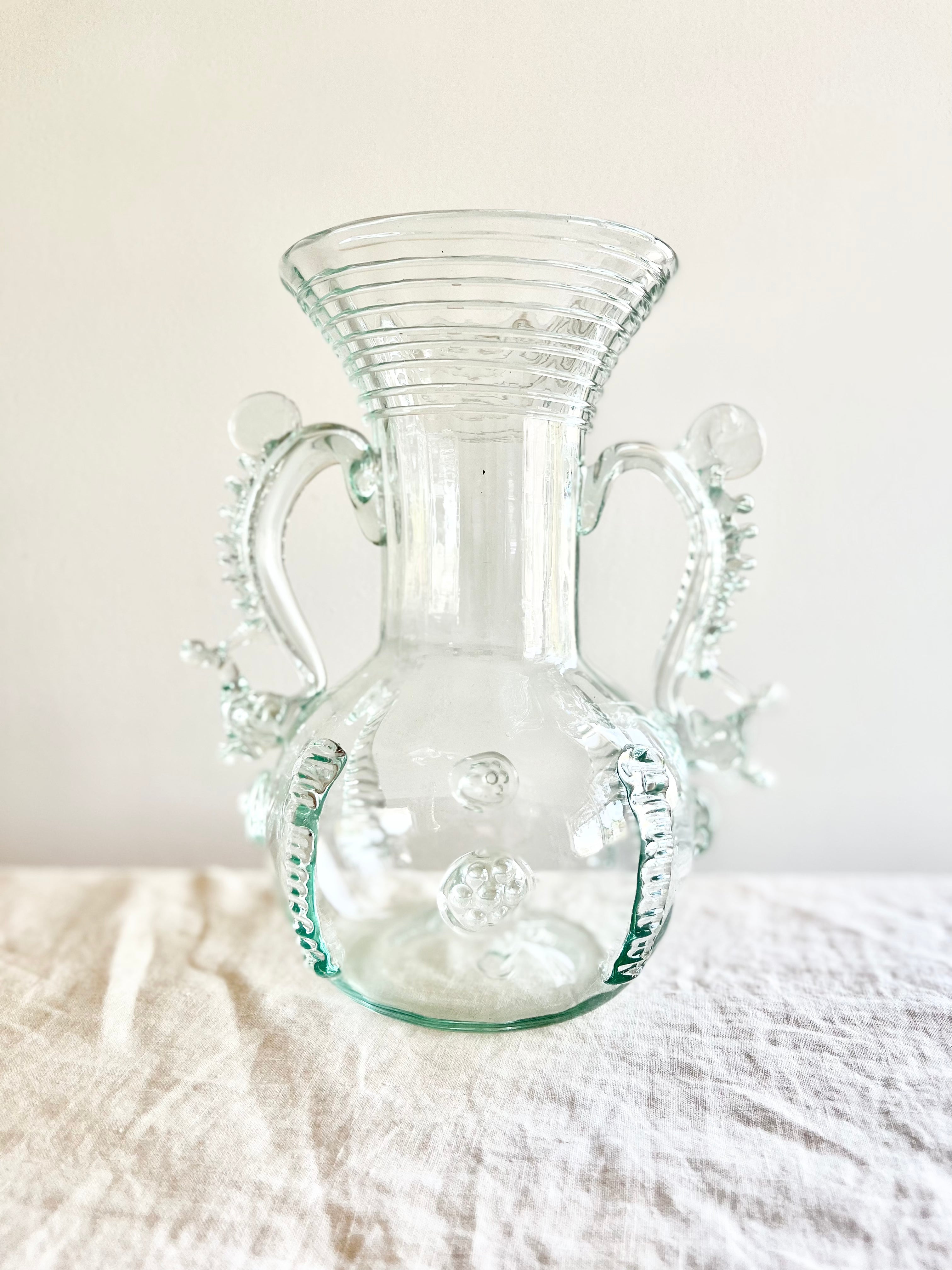 clear glass vase with two handles and clear glass stripes on neck 9.5 inches on white table