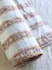 twin size white cotton quilt with gold, blue and pink floral stripes folded on bed