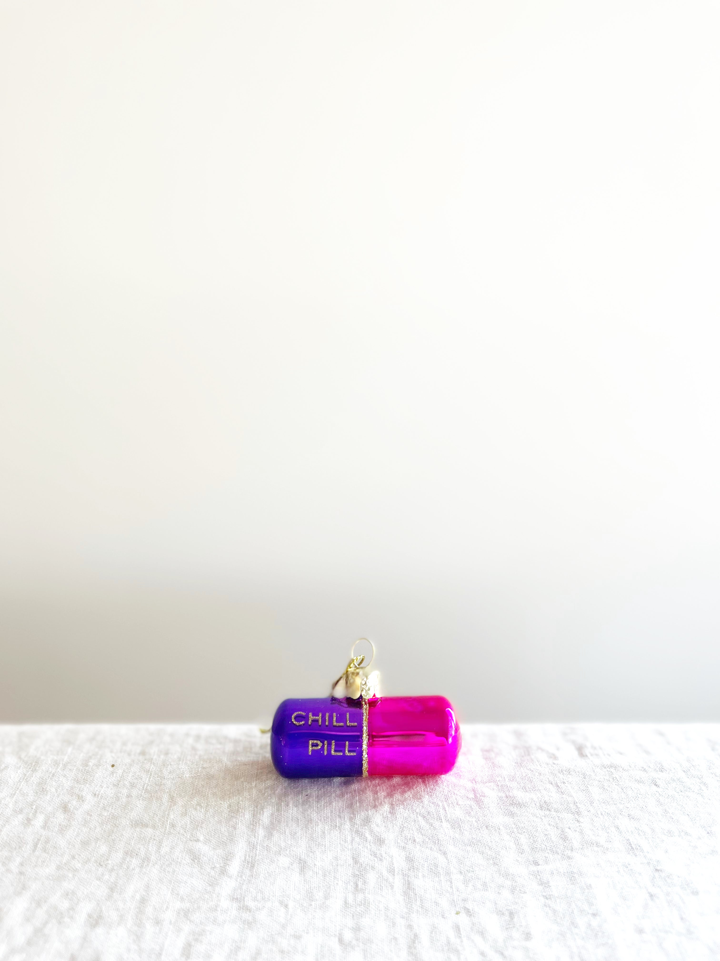 pink and purple glass christmas ornament shaped like a capsule with chill pill written on side alternate view