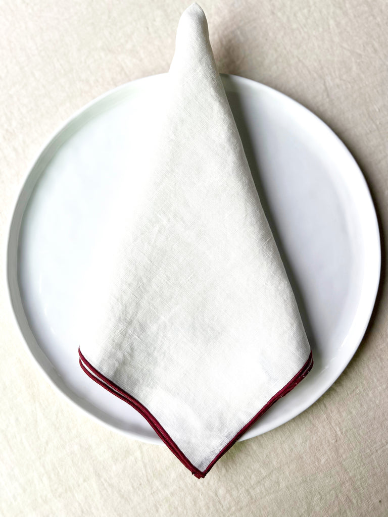 white rolled edge linen napkins with burgandy edge 18 inch square folded on white plate