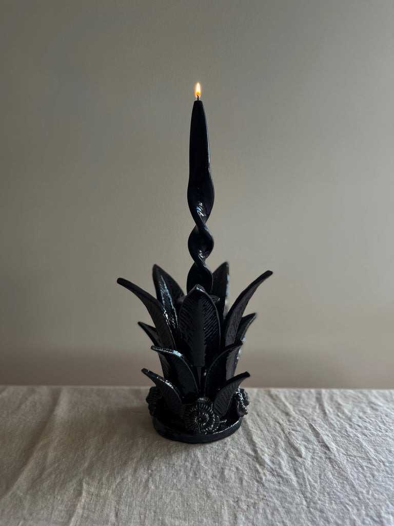 navy blue taper candle holder shaped like the top of a pineapple with lit blue candle