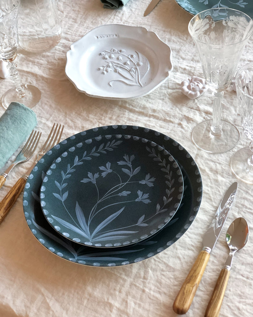 green dinner plate with hand painted white floral design in placesetting on linen tablecloth