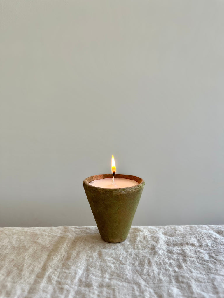 terra cotta candle with a mossy and aged green exterior small size on a table