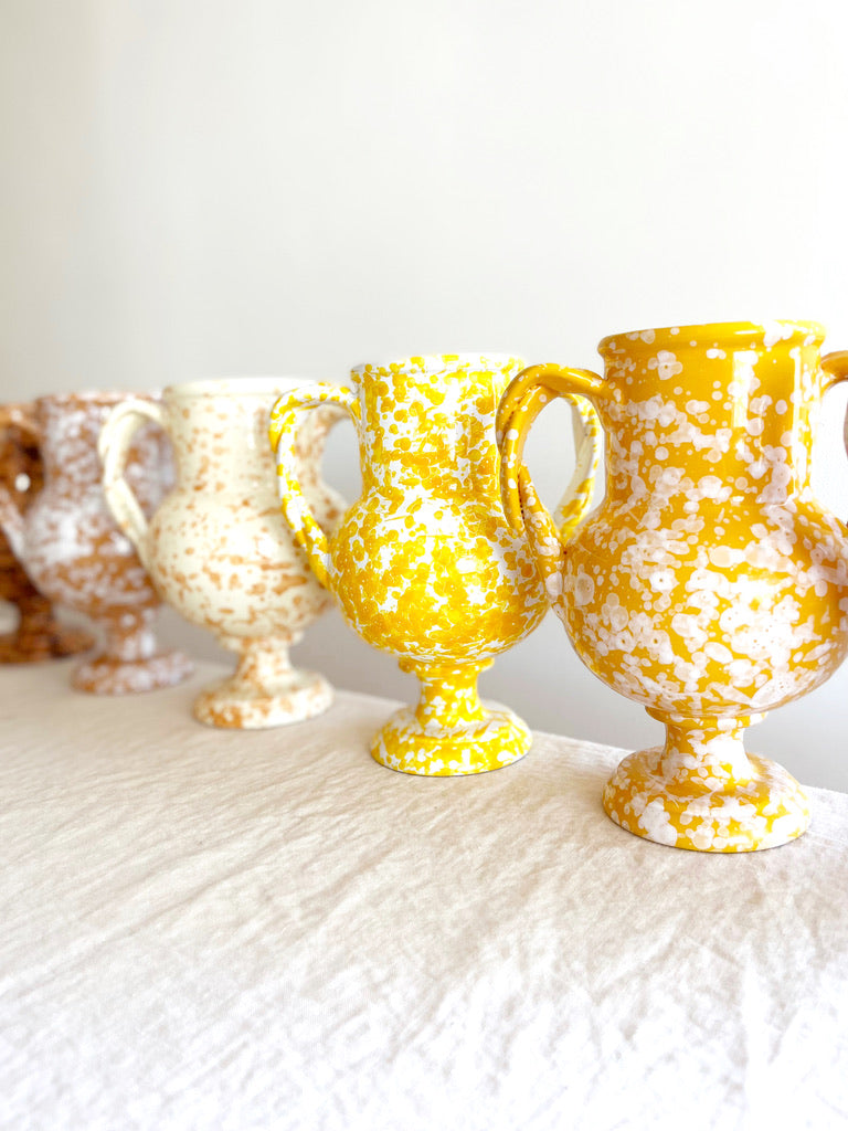 yellow amphora vase with white speckle pattern 13 inches tall on white table