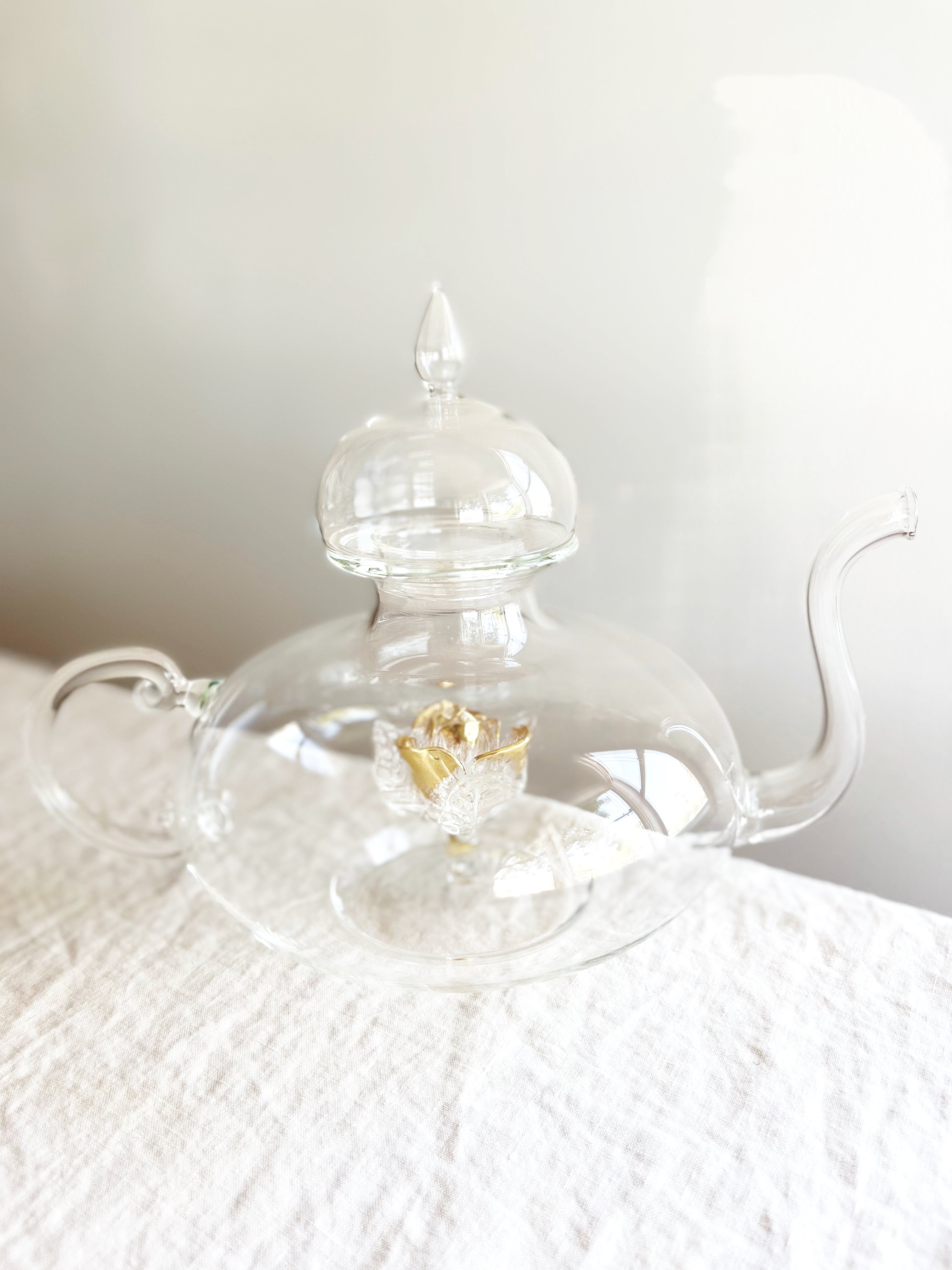 clear hand blown glass teapot with gold glass rose in bottom on table