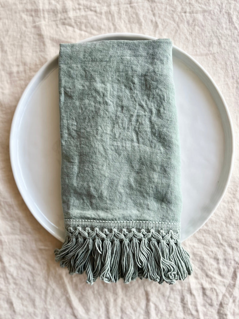 sage green linen napkins with fringe on white plate