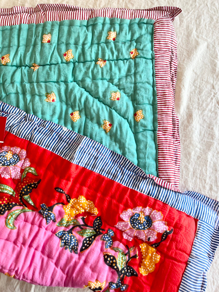 red and pink cotton quilt with pink and yellow flowers and a blue and white striped border 27 x 40 inches edge view