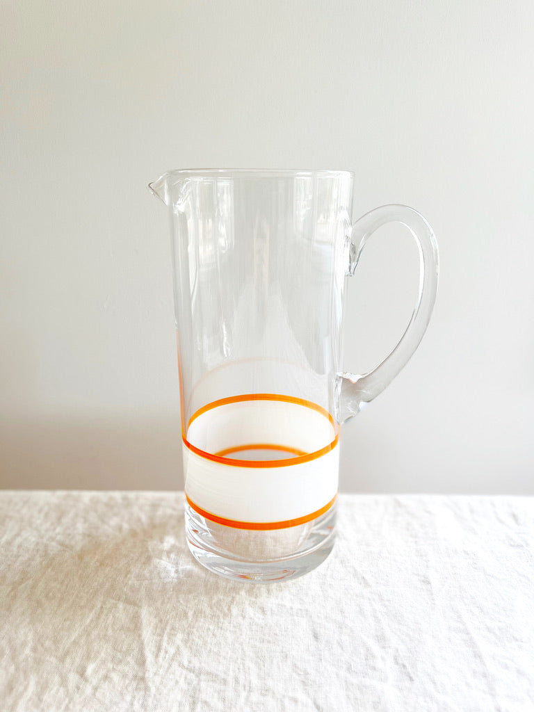 glass pitcher with hand painted white and orange stripes 10 inches tall on white table