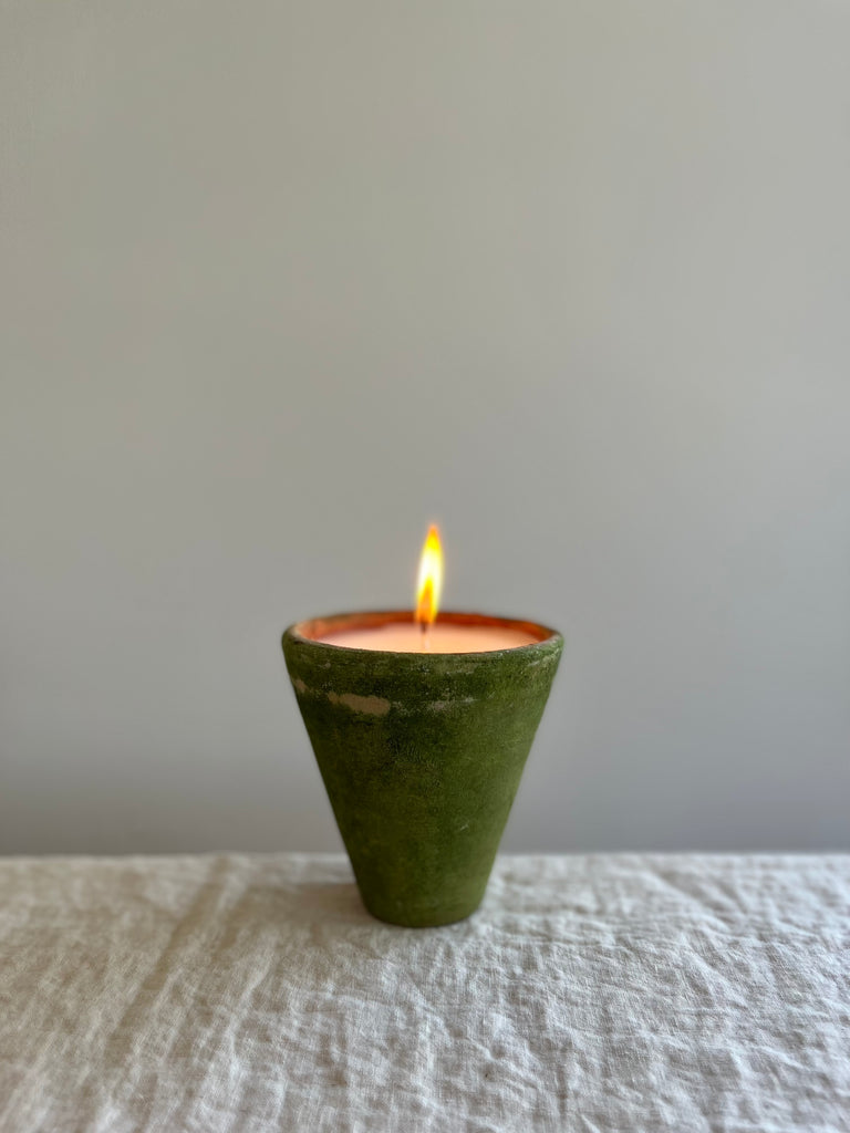 terra cotta candle with a mossy and aged green exterior on a table
