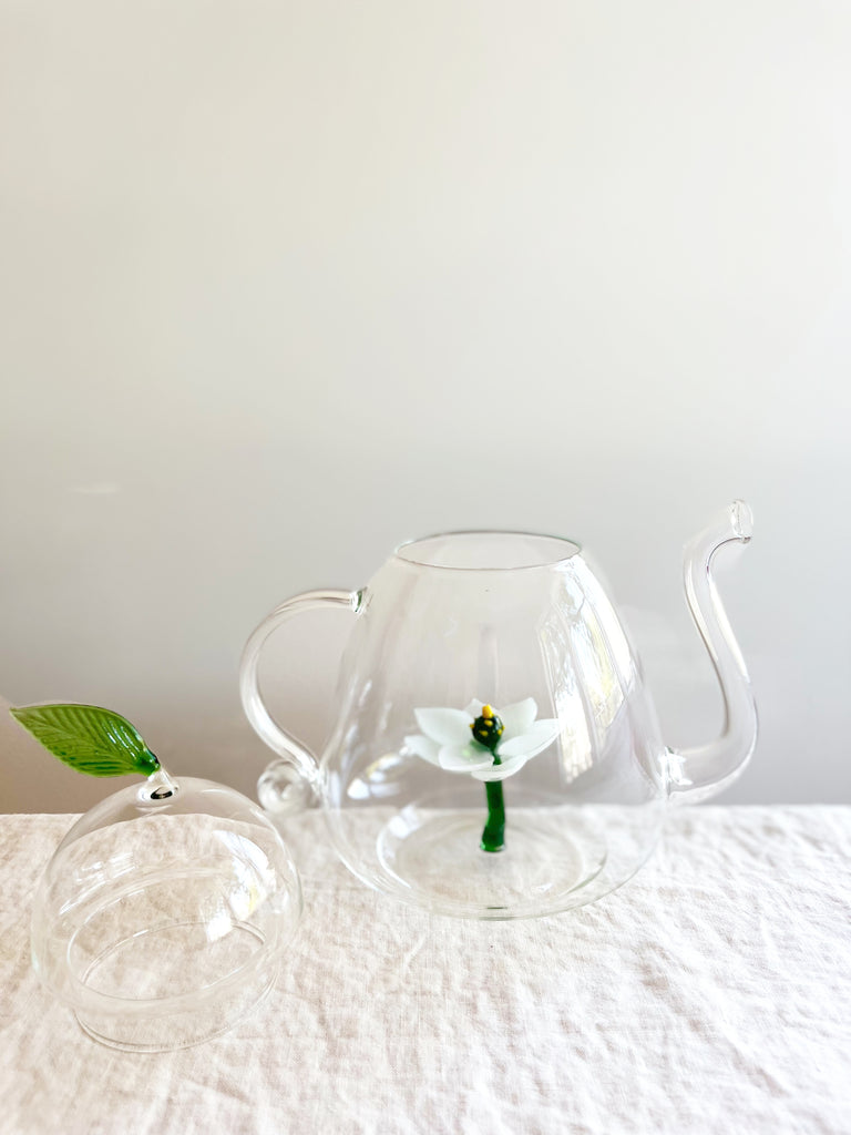 clear hand blown glass teapot with white glass lotus flower in bottom with leaf detail shown on lid