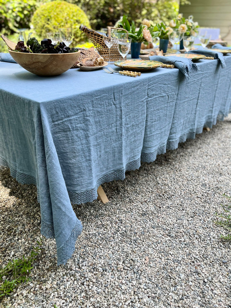 Blue Milano Macrame Tablecloth 74 inch shown hanging off of a table