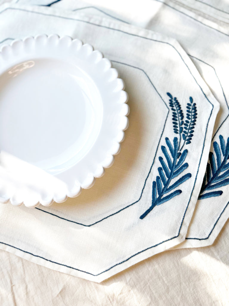 hand painted white dinner plate with scalloped edge on blue embroidered placemat