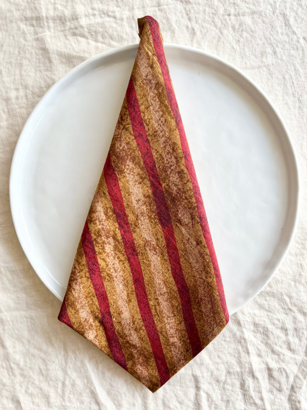 red gold and tan striped cotton napkin folded on plate