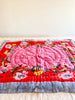 red and pink cotton quilt with pink and yellow flowers and a blue and white striped border 27 x 40 inches on bed
