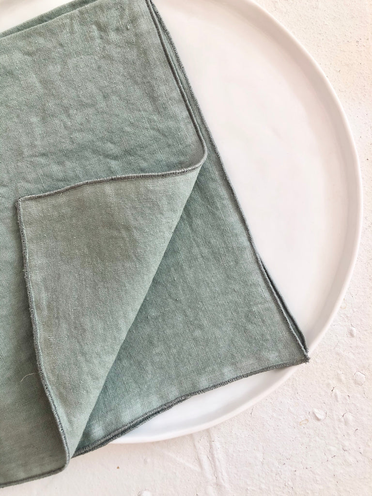 sage green rolled edge linen napkins 18 inch square folded on plate