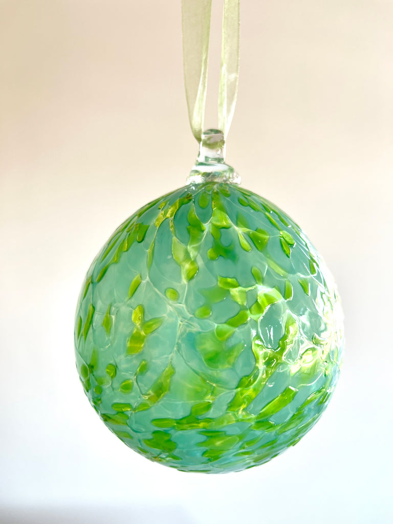 hand blown glass ornament with light and mint green speckle pattern hanging on ribbon