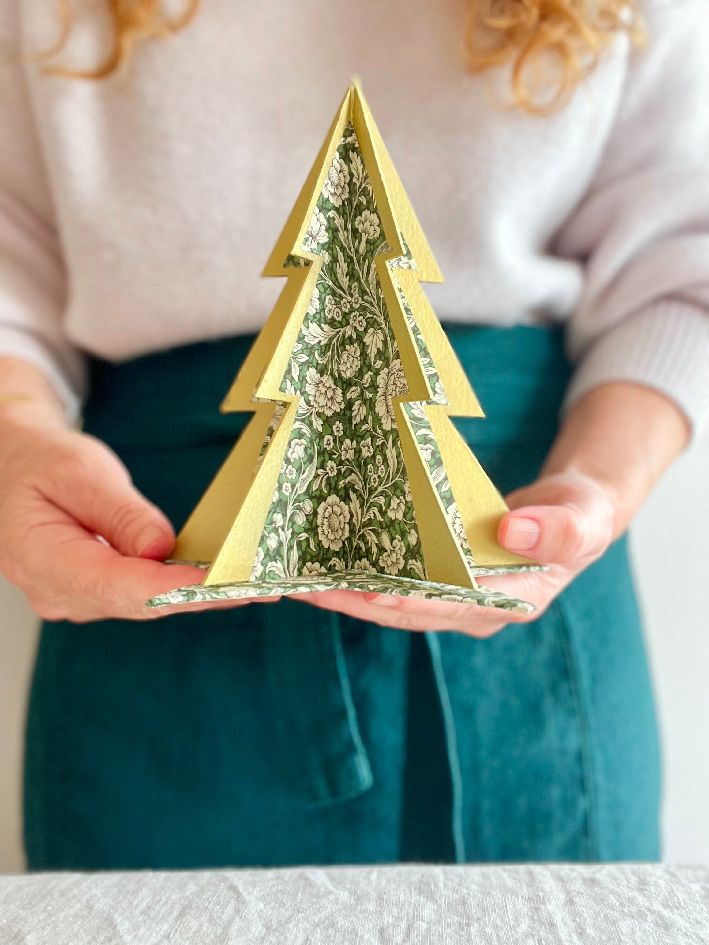 decorative Paper Christmas Tree stands with green and white chintz pattern held by woman