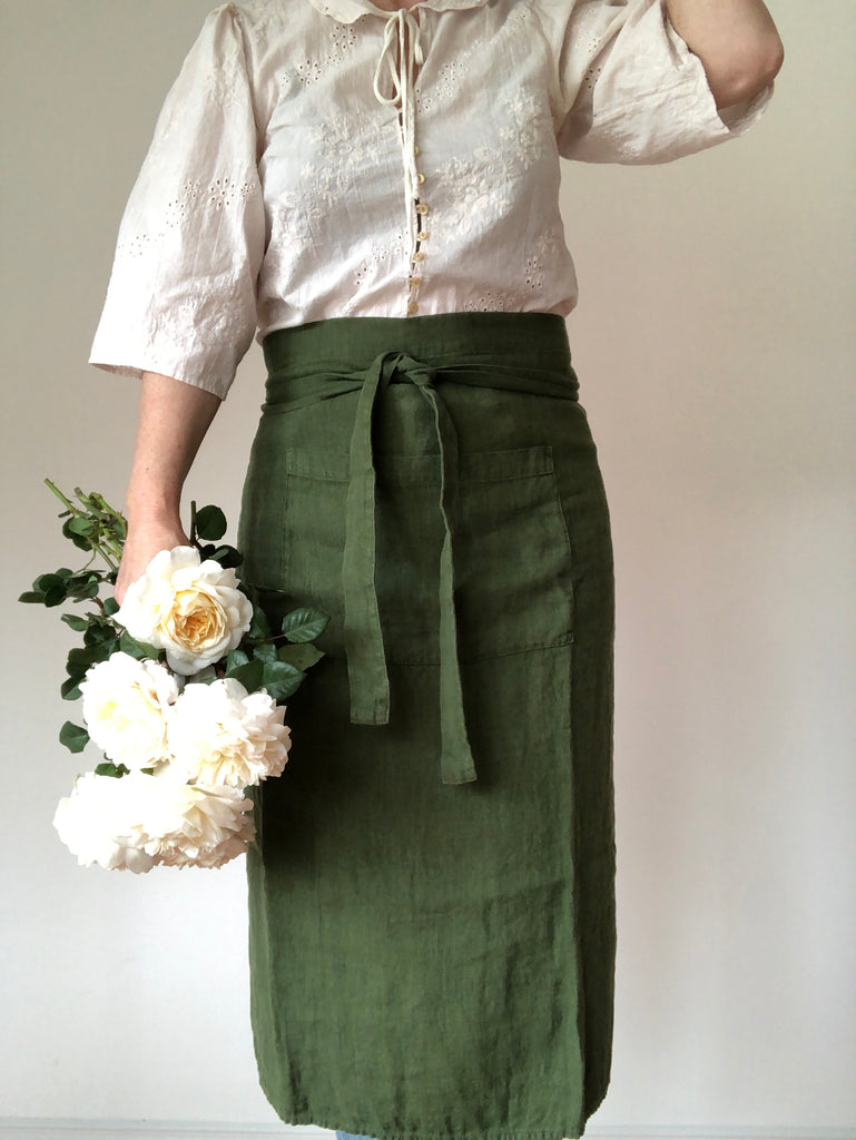 green linen apron bistro style worn by woman holding roses