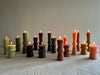 assorted totem candles light green dark green wine pink natural on a table with flame lit