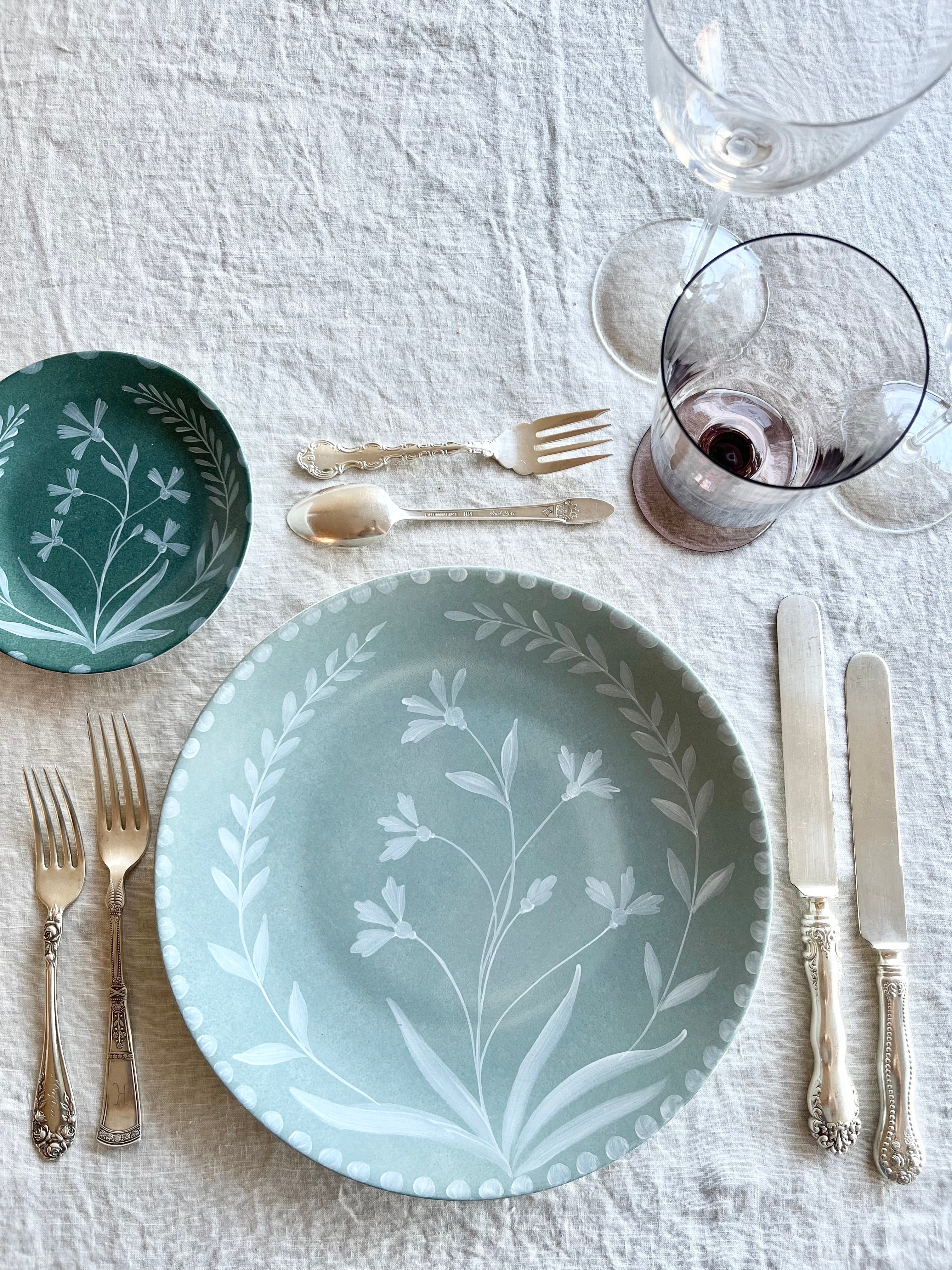 green bread plate with hand painted white floral design on linen tablecloth