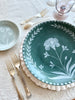 green dinner plate with hand painted white floral design on white charger