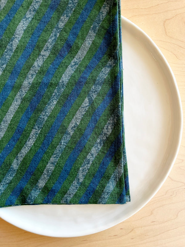 cotton napkin green with dark and light blue stripes laid over a white table
