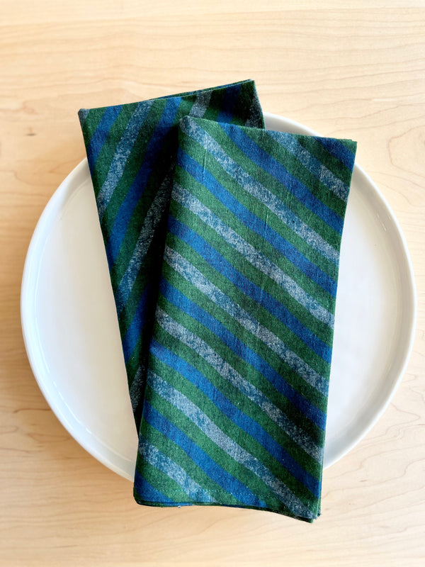 cotton napkins green with dark and light blue stripes laid over a plate on a wood table