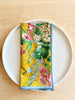 bright yellow cotton napkin with red floral print and light blue edge folded on plate