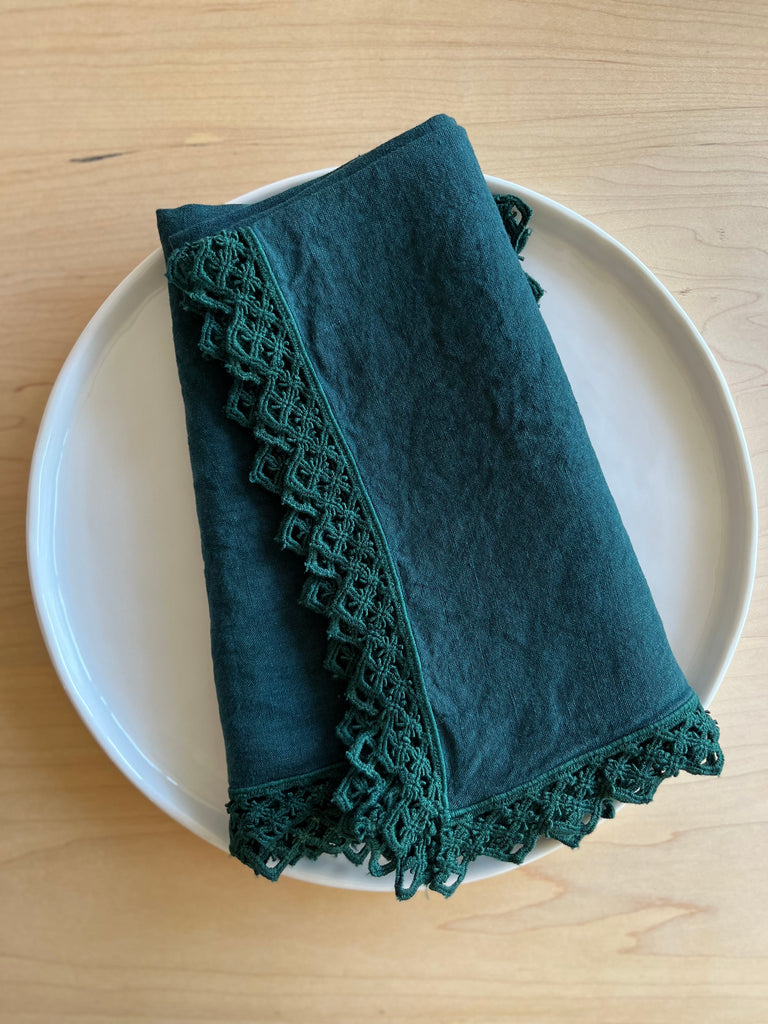 teal linen napkin with macrame trim folded on plate
