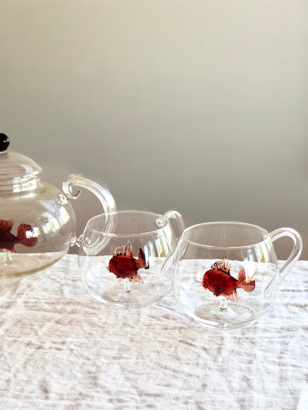clear hand blown glass tea cups with red glass fish in bottom on white table