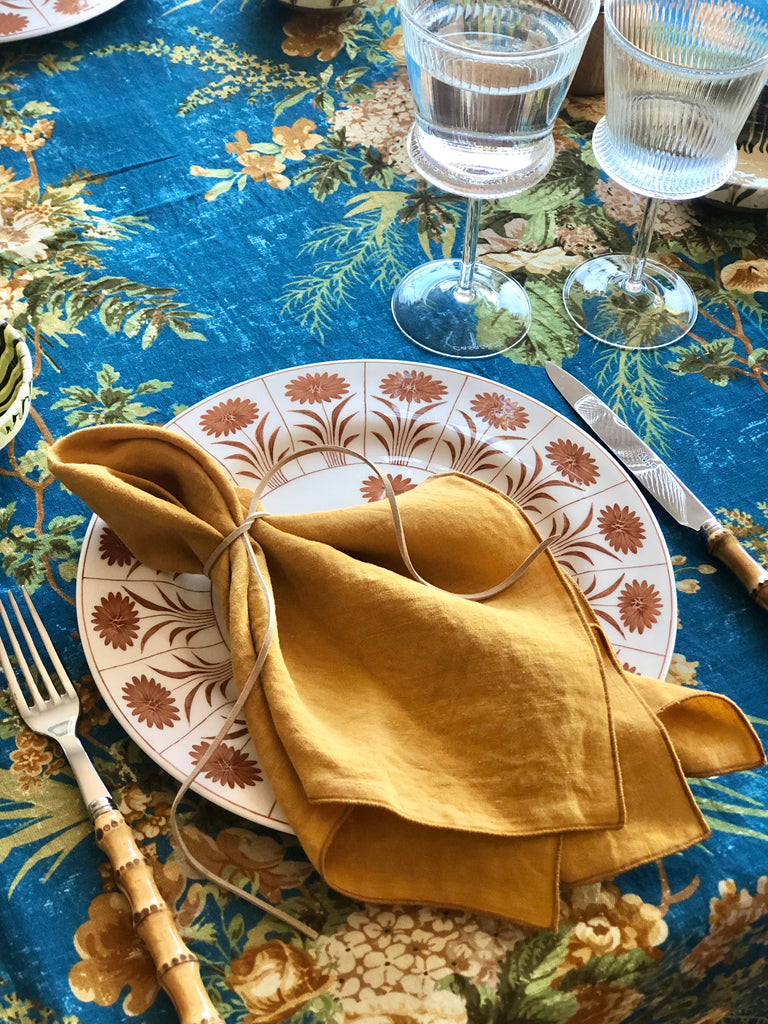 blue tablecloth with cream white and light brown floral pattern with gold napkin