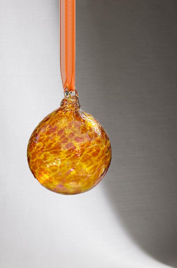 hand blown glass ornament with light and dark orange swirl pattern on white background