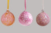 set of three hand blown glass ornaments in peach pink and mauve hanging from ribbons