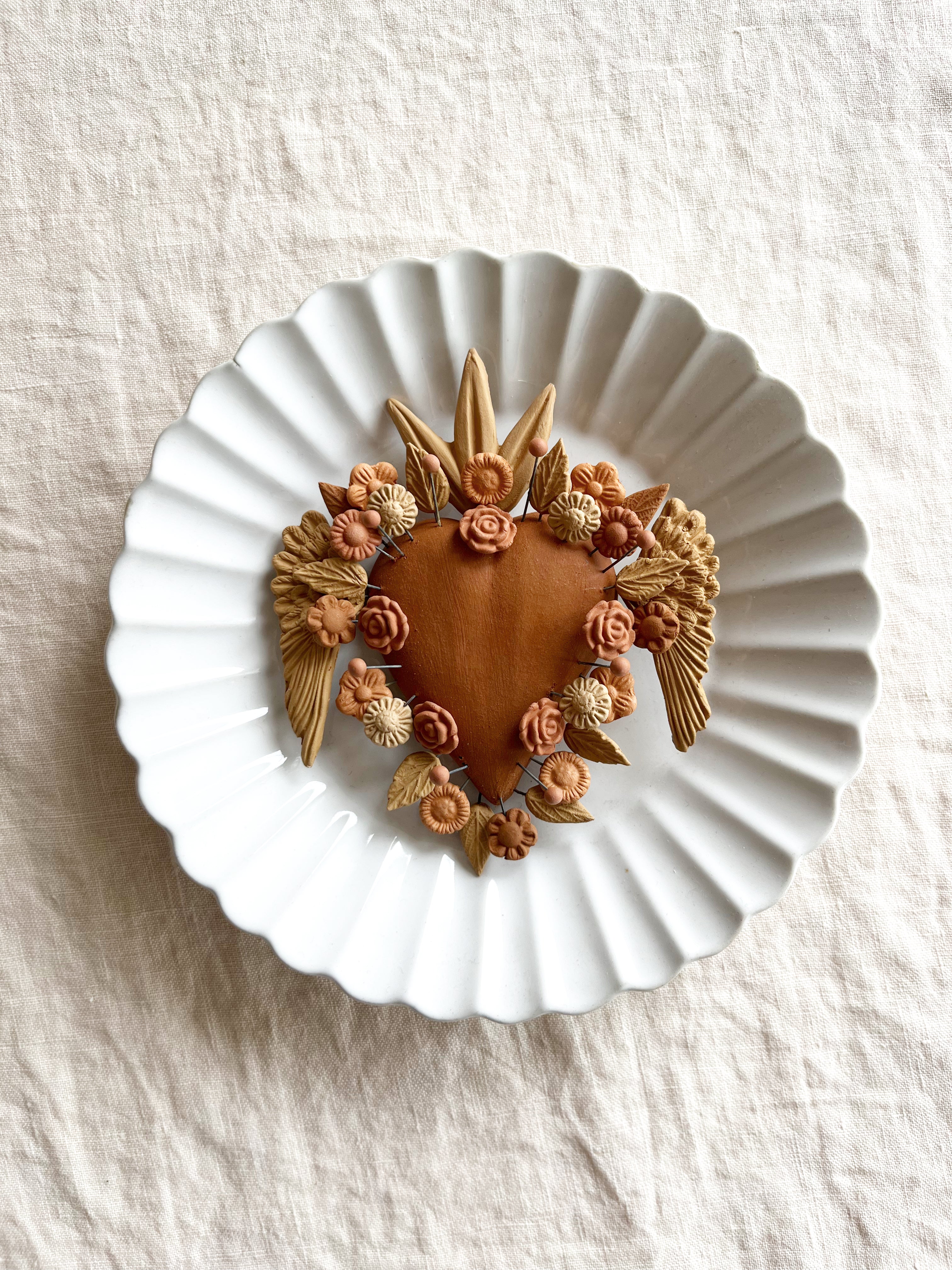 ceramic heart shaped christmas ornament with wings around the edge on white plate