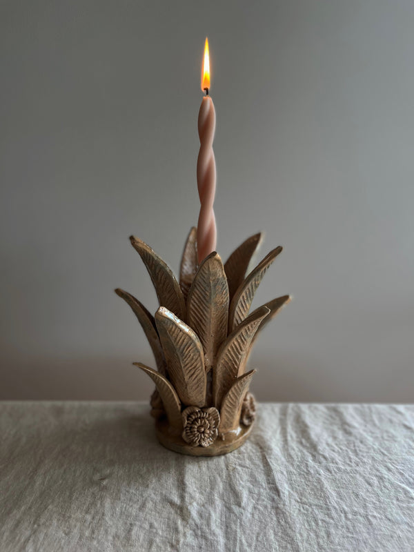 light brown taper candle holder shaped like the top of a pineapple with lit candle