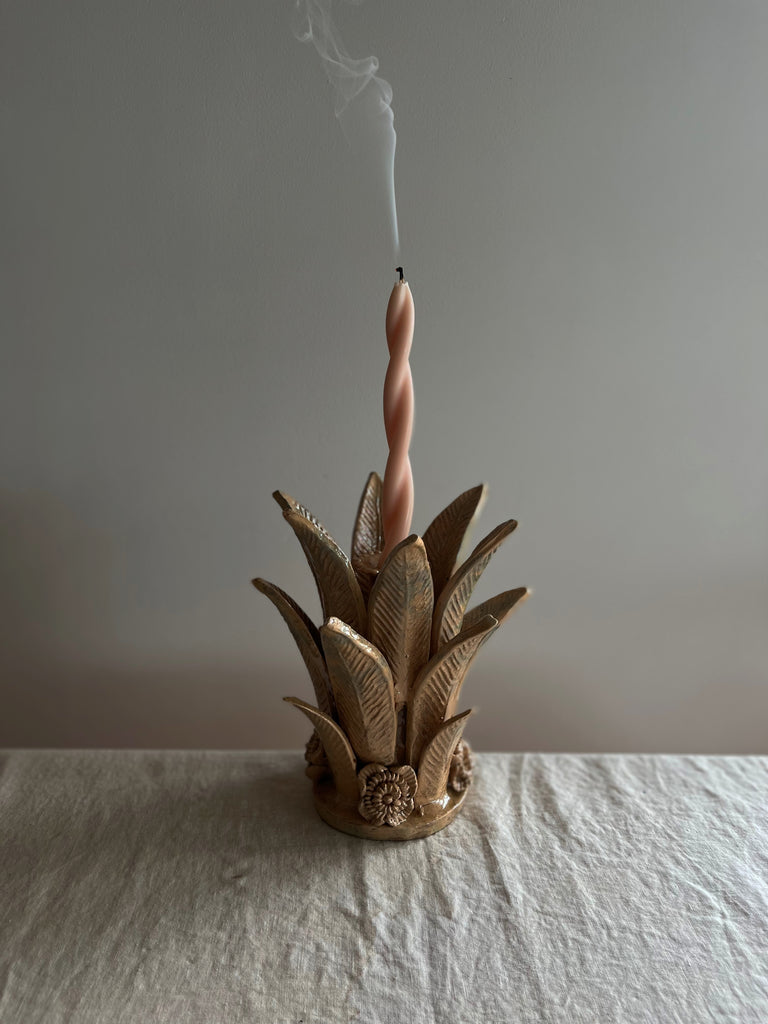 light brown taper candle holder shaped like the top of a pineapple with pink candle