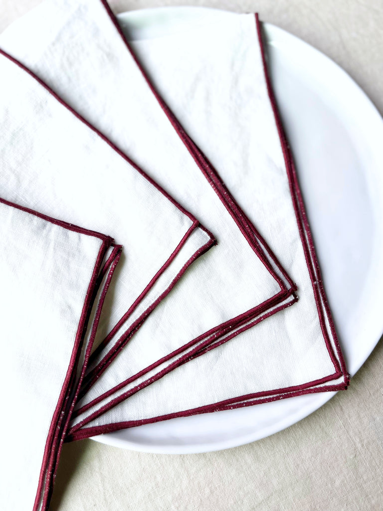 white rolled edge linen napkins with burgandy edge 18 inch square fanned out on table