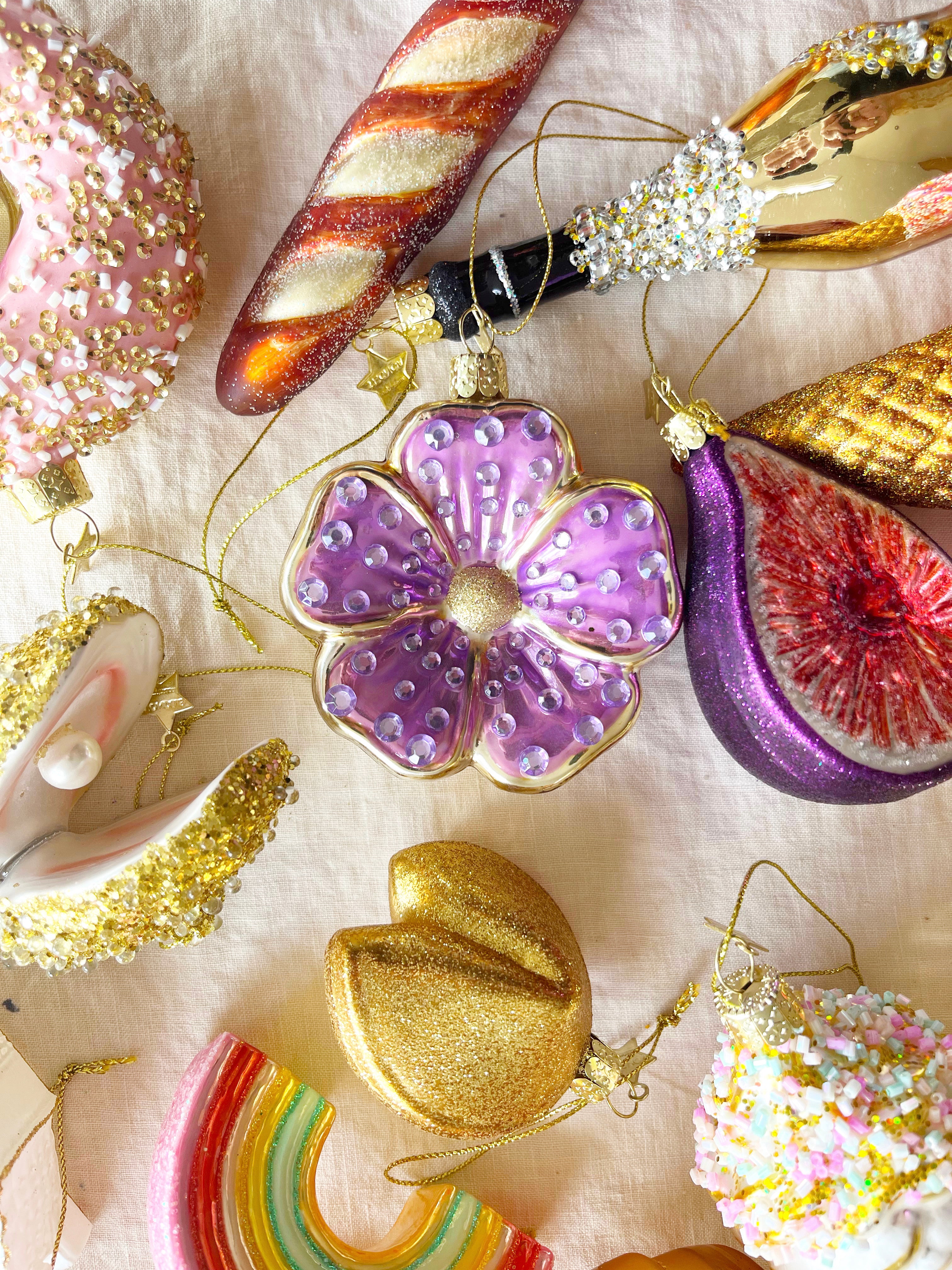 flower shaped glass christmas ornament in lavender on table with other ornaments