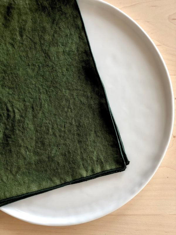 forest green rolled edge linen napkins with teal edge 18 inch square on a plate