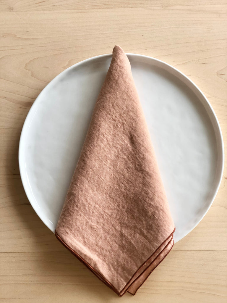 rolled edge linen napkins 18 inch blush color folded on a plate