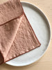 rolled edge linen napkins 18 inch blush color folded up on a plate